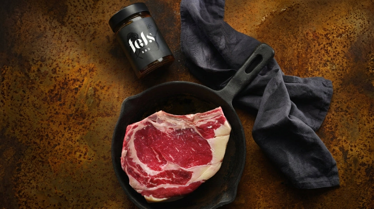 Nyers marha steak öntöttvas serpenyőben és FELS BBQ szósz üvegben – prémium alapanyagok BBQ receptekhez
